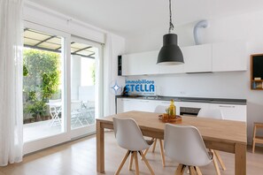 Una cucina moderna con mobili bianchi, un tavolo da pranzo in legno e una lampada a sospensione nera.