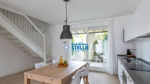 Une cuisine moderne dotée d’une cuisinière intégrée, un coin repas avec une table en bois et des chaises blanches, et un escalier menant à un niveau supérieur.
