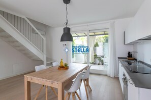Eine moderne Küche mit eingebautem Herd, ein Essbereich mit Holztisch und weißen Stühlen sowie eine Treppe, die in einen oberen Bereich führt.