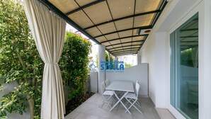 Une terrasse couverte, dotée d’une table et de chaises, entourée de verdure et bordée d’une paroi en verre.