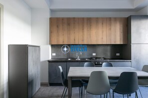 A modern kitchen with wooden cabinets, a stainless steel sink, and a dining area with a table and chairs. - Trento Apartment P.T. [100 mt from the beach] (Lido di Jesolo)
