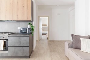 Eine moderne Küche mit Mikrowelle, Herd und Schränken, die in einen Wohnbereich mit Sofa und Pflanze übergeht.