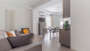Een moderne woonkamer met een bank, eettafel en stoelen. Er is een keuken met een aanrecht en een plant.