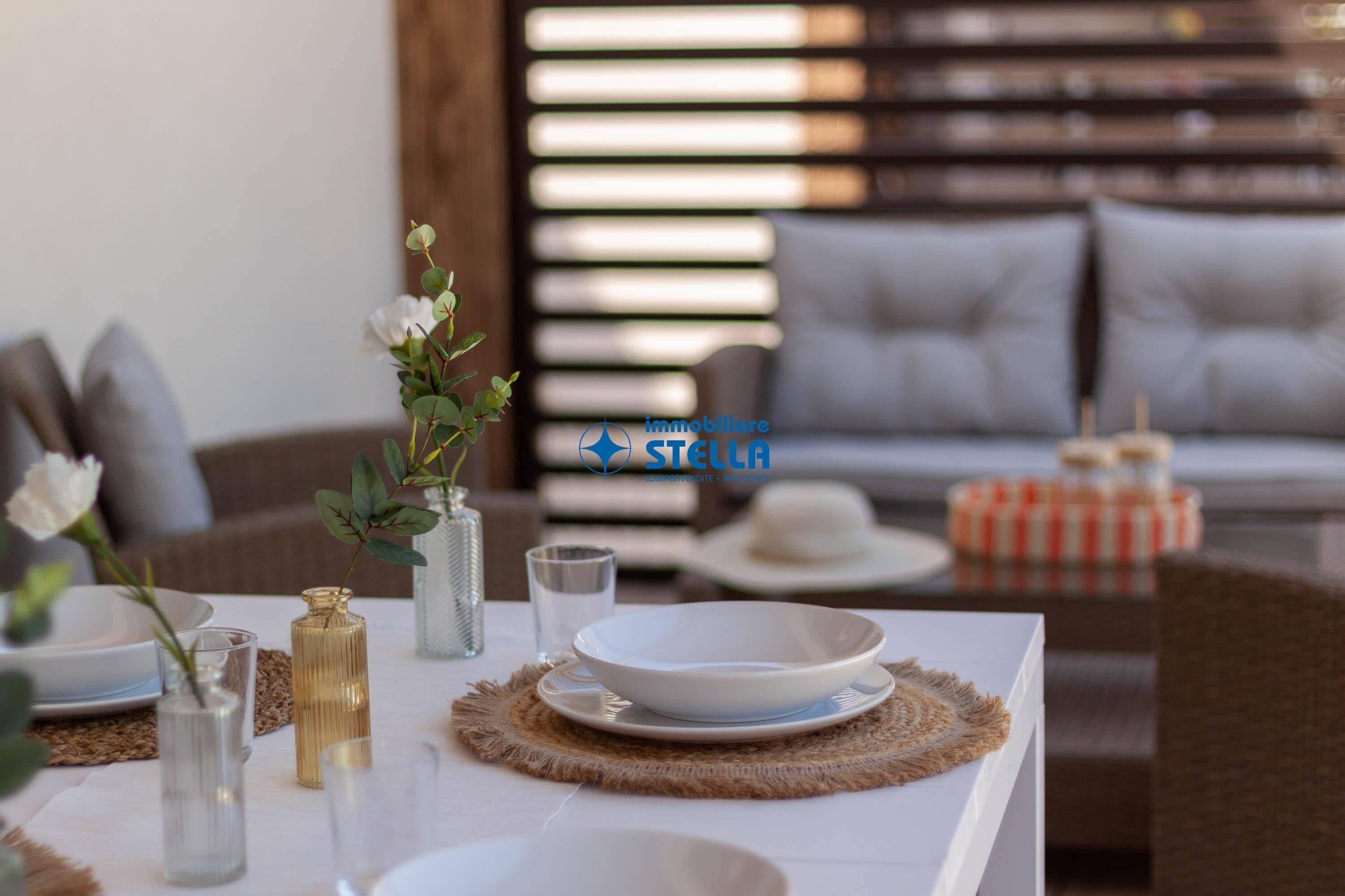Una mesa de comedor dispuesta con platos, vasos y un florero con flores.