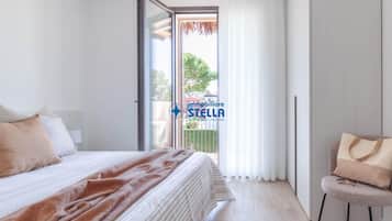 Un dormitorio con cama, una silla, ventana con cortinas y vistas al exterior.