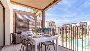 Un balcon avec une table à manger pour quatre personnes, un canapé et une vue sur une piscine et d’autres bâtiments.