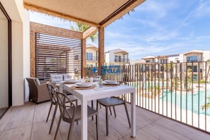 Un balcón con una mesa de comedor dispuesta para cuatro personas, un sofá y vistas a una piscina y otros edificios.