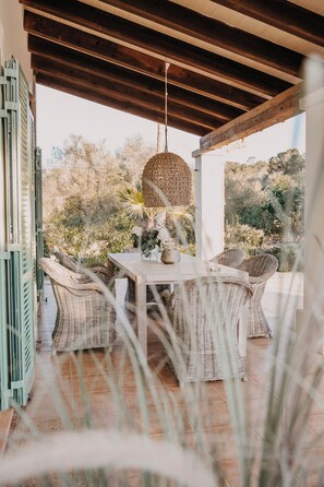 Eine Terrasse im Freien mit Korbmöbeln, einer Hängelampe und Blick auf die umliegende Landschaft.