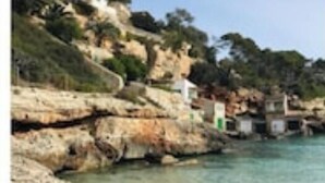 Ett kustlandskap med ett bergigt område, klart vatten och en sandstrand.