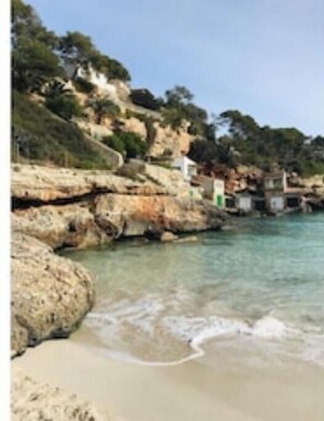 Eine Küstenlandschaft mit felsigem Gelände, klarem Wasser und einem Sandstrand.