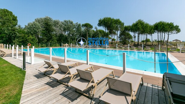 Ein Poolbereich mit Liegestühlen, einer Holzterrasse und blauem Himmel.