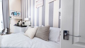 Habitación de hotel con cama, microondas, una mesita con tetera y un estante en la pared con un cuadro enmarcado.