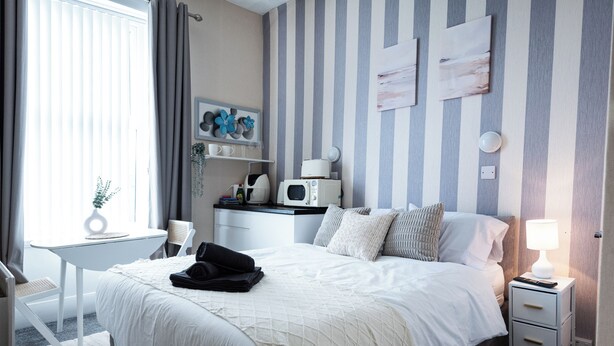 Habitación de hotel ordenada con cama, mesita de noche, silla y una pequeña mesa con microondas.