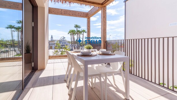 Ein Balkon mit einem weißen Esstisch, einem Blumentopf und Blick auf Palmen und ein entferntes Gebäude.