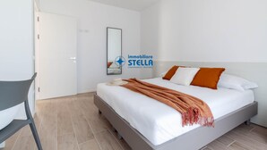 Ein Schlafzimmer mit einem Bett, einem Sessel, einer Tür und einem Wandspiegel.