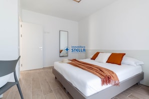 Un dormitorio con cama, una silla, una puerta y un espejo fijado a la pared.
