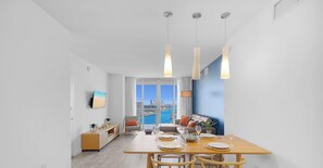 A modern dining area with a wooden table, chairs, and hanging pendant lights. - 1BR · Intracoastal View · Full Amenities · W/D (Hallandale Beach)