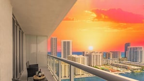 Un balcon offrant une vue sur les toits d’une ville au coucher du soleil, une table à manger avec des chaises et une piscine.