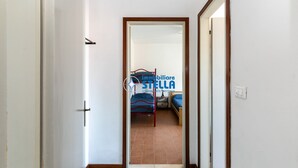 A corridor leading to a bedroom with a bed, a nightstand, and a chair. - Romeo # three-room apartment 19# with beach space° (Lido di Jesolo)