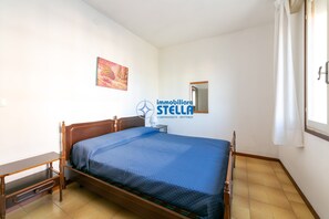 Ein Schlafzimmer mit einem hölzernen Bett, einem Nachttisch, einer kleinen Nachttischlampe, einem Wandspiegel und einem Gemälde.
