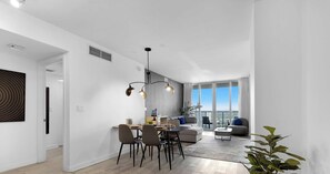 A modern interior with a dining area, a sofa, and a view of the city. - 2BR Resort Condo  High Floor Marina Views (Hallandale Beach)