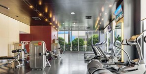 A gym with cardio machines, weight machines, and a large window with a view of greenery. - Elegant Studio, Bay View & Resort Pool (Hallandale Beach)