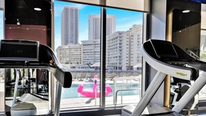 Un gimnasio con equipo de ejercicio y vistas a un paisaje urbano a través de amplios ventanales.