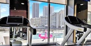 A gym with treadmills and a view of a pool and buildings. - High-Floor Beachwalk Studio | Bay View Balcony (Hallandale Beach)