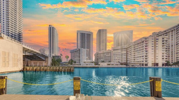 Zona de comedor junto al agua, con vista al horizonte de la ciudad, un muelle y señales de precaución.