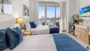 Habitación de hotel con dos camas, un escritorio, un televisor y vista a la ciudad.