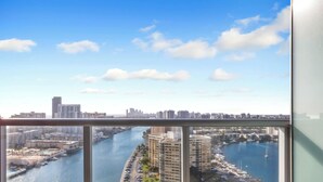 A balcony with a city view overlooking a river, a marina, and high-rise buildings. - Sweeping Sunset Views -2BR Beachwalk Resort (Hallandale Beach)