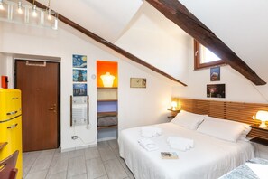 A bedroom with a bed, bedside lamps, a wooden headboard, a shelf with artwork, and a door. - GuestHost - La Mansarda di Garibaldi (Turin)