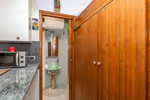 Eine Küche mit Mikrowelle, einem roten Apfel und einer Holztür, die zu einem Badezimmer mit Waschbecken und Spiegel führt.