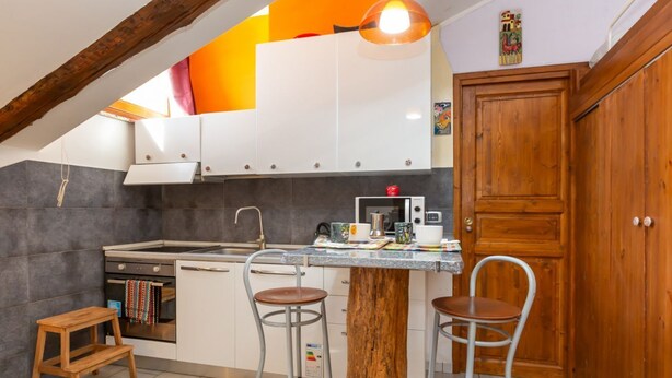 Una cocina con una mesa de madera, dos taburetes de bar, una estufa y armarios.