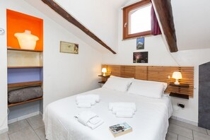 Ein Schlafzimmer mit einem Bett, Nachttischlampen, einem Fenster und einem Regal mit einer Vase.