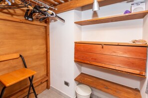 Ein kleines Zimmer mit einer Holzbank, einem Holzkasten und einem weißen Eimer auf dem Boden.