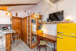 Eine kompakte Küche mit einem Holzkasten, einem kleinen Esstisch, einem gelben Kühlschrank und einem Fernseher auf einem Regal.