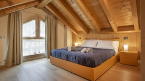 Une chambre à coucher avec un plafond en bois, un lit doté d’une tête de lit, une table de chevet et une fenêtre avec des rideaux.