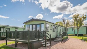 A row of green mobile homes with a wooden deck and steps leading to the entrance. - St Andrews Holiday Park | Harbour Reach (No 11) (St Andrews)