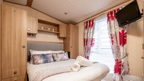 A bedroom with a bed, wooden wardrobe, built-in shelves, a television, and a window with curtains. - St Andrews Holiday Park | Harbour Reach (No 11) (St Andrews)