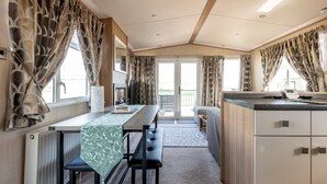 A compact kitchen with a dining area, a bench, and a view through the glass door. - St Andrews Holiday Park | Harbour Reach (No 11) (St Andrews)