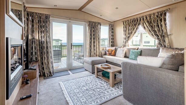 A living room with a sofa, a coffee table, a TV, and a sliding glass door leading to an outdoor balcony. - St Andrews Holiday Park | Harbour Reach (No 11) (St Andrews)