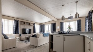 A modern living room with a flat-screen TV, a sofa, a coffee table, and a kitchen area with a countertop and cabinets. - Lodge No 138 | Stewarts Resort Cameron (Cameron)