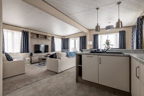 Ein modernes Wohnzimmer mit Flachbildfernseher, einer Couch, einem Couchtisch und einer Küchenzeile mit Arbeitsplatte und Schränken.