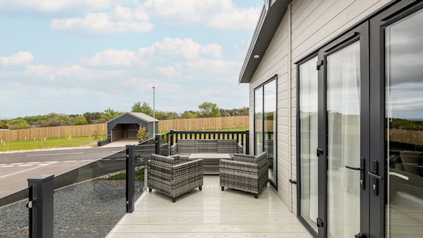 A modern outdoor patio with a built-in seating area, a wooden fence, and a view of the road and greenery in the background. - Lodge No 138 | Stewarts Resort Cameron (Cameron)