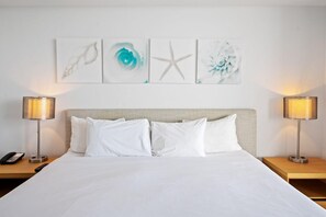 A hotel room with a large bed, two bedside tables, a telephone, and wall art. - Bright Apt, Intracoastal View | Balcony & Pool (Hallandale Beach)