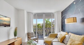 Ein modernes Wohnzimmer mit einer Couch, einem Sessel, einem Fernseher und einem großen Fenster.