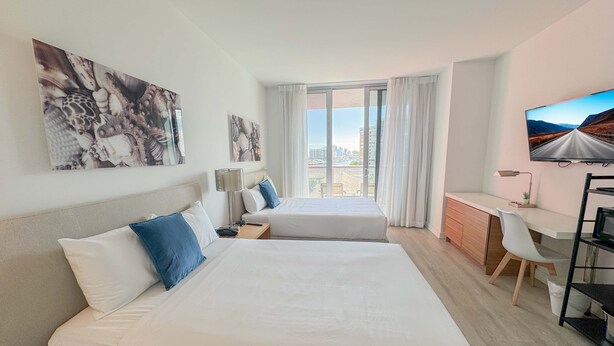 Ett hotellrum med två sängar, ett skrivbord, en TV och en balkong med utsikt över staden.