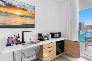 A compact kitchenette with a coffee maker, microwave, and a view of a sunset over water. - Premium Floor · 2BR · Intracoastal · Beachwalk (Hallandale Beach)