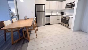 Een moderne keuken met een roestvrijstalen koelkast, magnetron en oven. Er is een eettafel met stoelen en een klein keukeneiland.